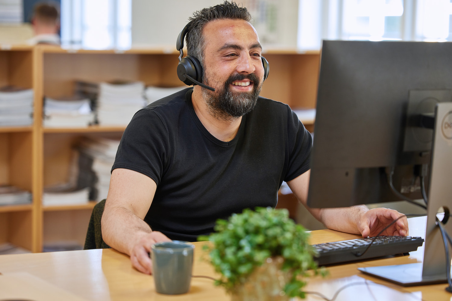 A man is sitting with headphones on in front of his computer at a desk.