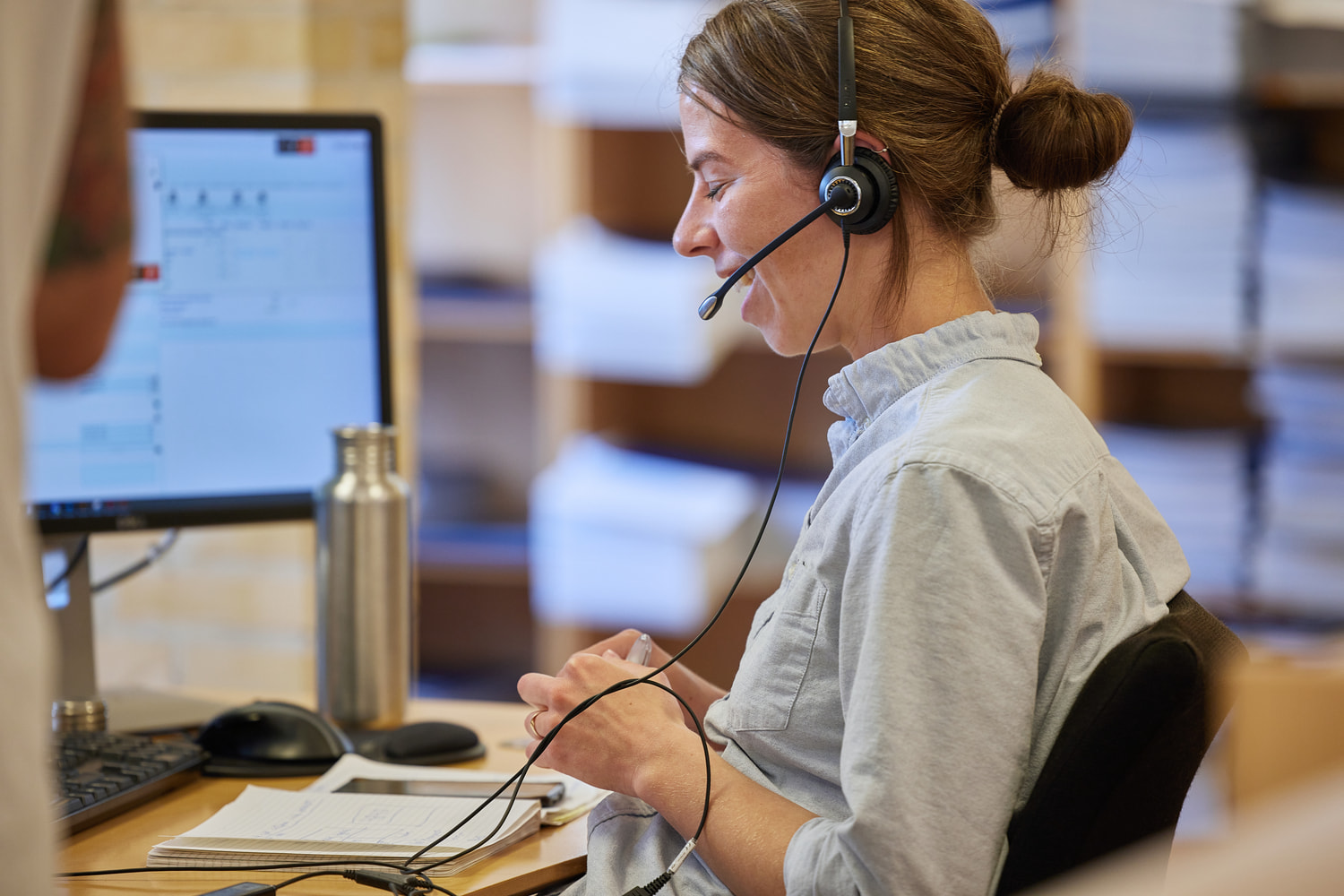 An employee from the communication team wearing headphones while sitting at a desk and talking with a customer.