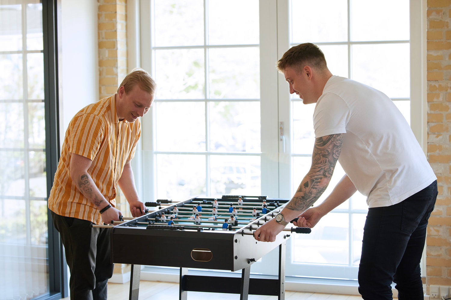 Two men are playing football at JS Danmark while smiling and having fun.
